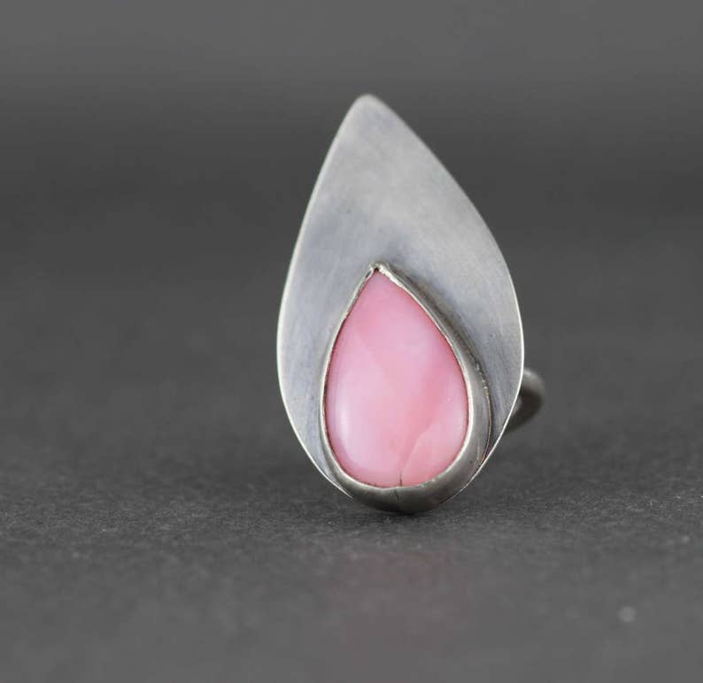 May include: A silver ring with a teardrop-shaped pink opal gemstone set in a silver bezel.