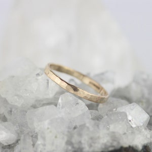 K&ouml;nnte beinhalten: Ein d&uuml;nner goldener Ring mit geh&auml;mmerter Textur. Der Ring liegt auf einem Bett aus wei&szlig;en Kristallen.