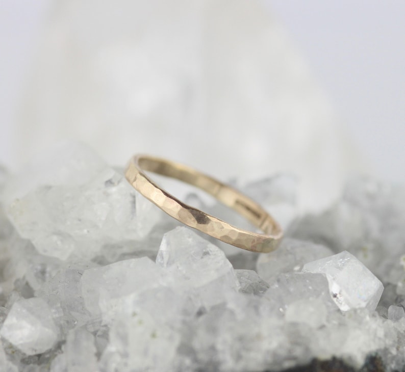 K&ouml;nnte beinhalten: Ein d&uuml;nner goldener Ring mit geh&auml;mmerter Textur. Der Ring liegt auf einem Bett aus wei&szlig;en Kristallen.