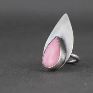 May include: A silver ring with a pink teardrop-shaped gemstone set in a leaf-shaped design.