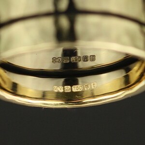 May include: Close-up of the inside of a gold ring with the markings "M 750" and "M 925" on the band.