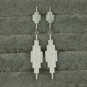 May include: A pair of silver geometric dangle earrings with a linear design. The earrings are long and narrow, with a pointed tip at the bottom.