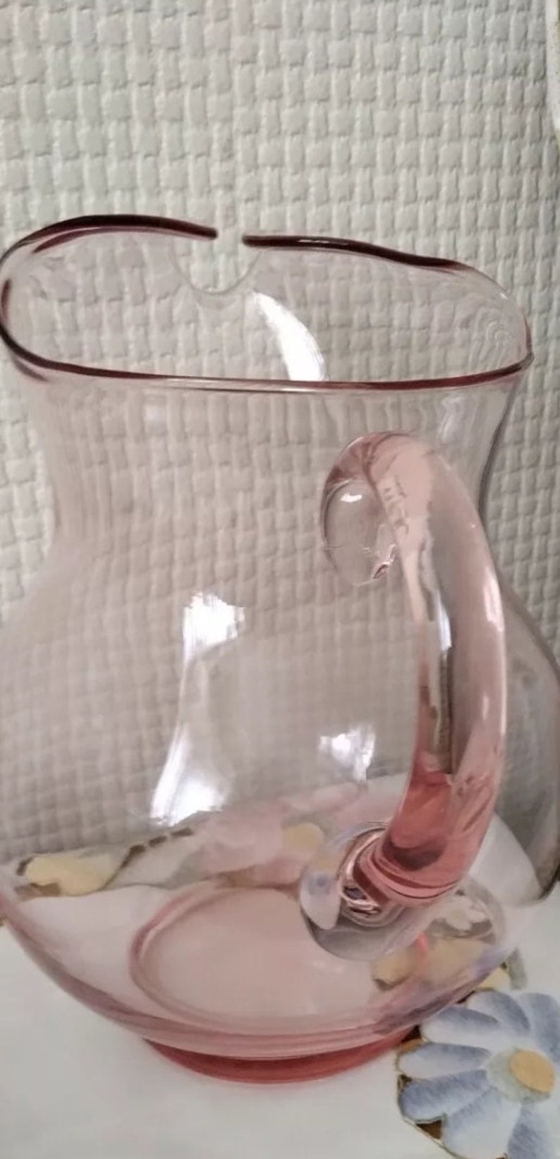 May include: A pink glass pitcher with a rounded body and a handle. The pitcher has a slightly frosted appearance.