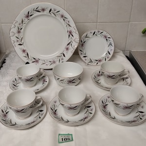 May include: A set of white teacups and saucers with a floral pattern in shades of pink and green. The set includes a larger plate and a bowl.