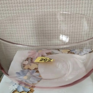 May include: A large, clear glass bowl with a pink tint. The bowl is sitting on a white surface with a floral pattern.