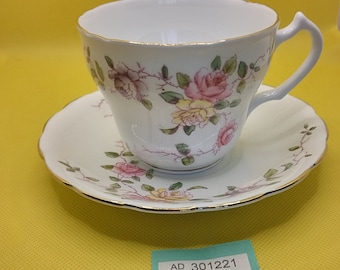 Può includere: Una tazza da tè e un piattino bianchi con un motivo floreale di rose rosa e gialle. Il piattino ha un bordo dorato. La tazza da tè ha un manico e un bordo dorato.