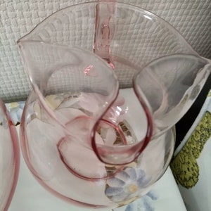 May include: A pink glass pitcher with a handle and a floral design. The pitcher is made of clear glass with a pink tint.