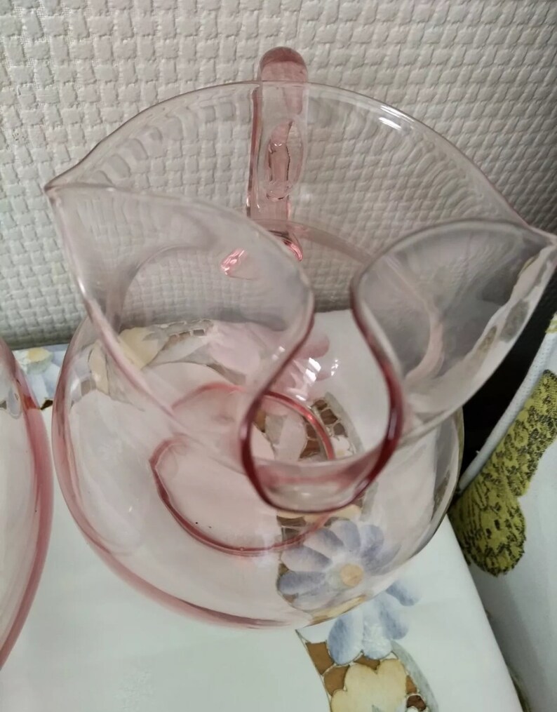 May include: A pink glass pitcher with a handle and a floral design. The pitcher is made of clear glass with a pink tint.