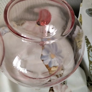 May include: A clear glass bowl with a pink tint. The bowl has a round shape and a smooth, polished surface. The bowl is empty.
