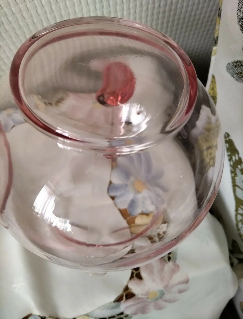 May include: A clear glass bowl with a pink tint. The bowl has a round shape and a smooth, polished surface. The bowl is empty.