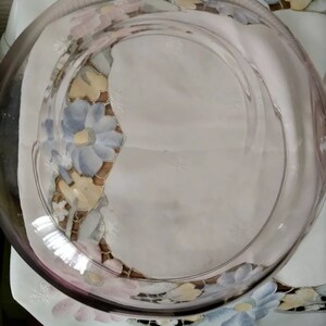 May include: A clear glass serving dish with a light pink rim. The dish is sitting on a white tablecloth with a floral pattern.