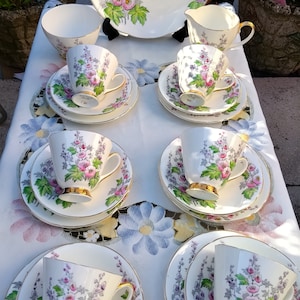 May include: A set of vintage teacups and saucers with a floral pattern. The cups and saucers are white with a pink and purple floral design. The set includes a teapot, creamer, and sugar bowl.