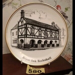 May include: A white ceramic plate with a gold rim features a black and white illustration of the Royal Oak Eccleshall pub. The plate is on a stand with a yellow price tag that reads "580".