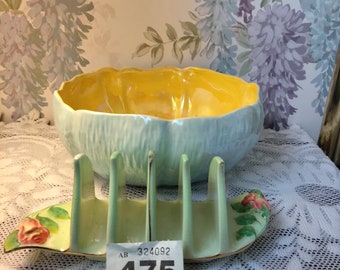 May include: A green and yellow ceramic bowl with a floral design and a matching green ceramic bread and butter plate with a floral design. The bowl and plate are on a white lace tablecloth. The price tag reads "475".