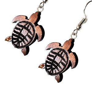 May include: A pair of wooden turtle earrings with a brown finish and black etched details. The earrings are on a silver hook.