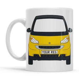 Pode incluir: Caneca de cerâmica branca com um design de carro Smart amarelo, teto preto e o texto "YOUR REG" na placa. O carro tem detalhes pretos e faróis.