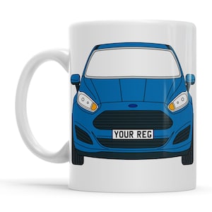 Op de afbeelding: Witte keramische mok met een blauw auto-ontwerp. De voorkant van de auto heeft koplampen, een grille en een kentekenplaat met "YOUR REG". De mok heeft een wit handvat en een glanzende afwerking.