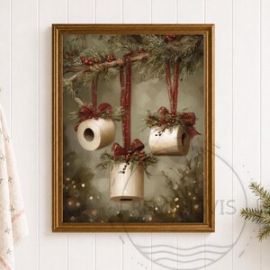 Könnte beinhalten: Ein gerahmter Wandkunstdruck, der drei Toilettenpapierrollen zeigt, die an immergrünen Zweigen hängen. Jede Rolle ist mit einer roten Schleife und roten Beeren verziert. Der Hintergrund zeigt eine weiche, verschwommene Waldszene mit Lichteffekten.