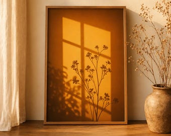 Pode incluir: Uma impressão de arte de parede retangular numa moldura de madeira com um fundo em tons de âmbar quente e a silhueta escura de um caule de flor silvestre. A imagem exibe a sombra de uma moldura de janela projetada na superfície.