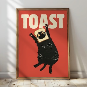 Könnte beinhalten: Gerahmter Kunstdruck mit einer schwarzen Katze mit Toast auf dem Kopf, vor rotem Hintergrund. Das Wort "TOAST" steht in großen, weißen Buchstaben über der Katze. Das Kunstwerk hat einen skurrilen und verspielten Stil.