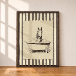 May include: A framed wall art print featuring a sketch of a horse sitting in a clawfoot bathtub filled with bubbles. The central image is set against a beige background with a scalloped edge, framed by vertical dark brown and cream stripes.