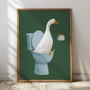 Pode incluir: Impressão artística emoldurada com um ganso branco sentado numa sanita azul sobre um fundo verde escuro. O ganso tem bico e patas amarelas. Um rolo de papel higiénico está montado na parede. A moldura é de cor castanha quente.