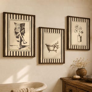 May include: Three framed wall art prints featuring black and white illustrations on a cream background with dark vertical stripes. The left print shows a person reading a newspaper on a toilet, the centre shows legs in a bathtub, and the right shows flowers.