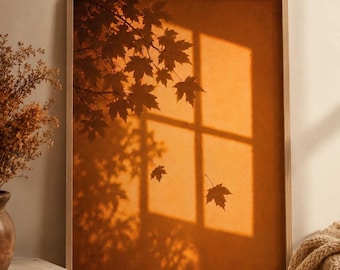 May include: A rectangular wall art print in a light wood frame featuring a warm orange background with the dark silhouette of maple tree branches and leaves cast by a window, including two individual falling leaves in the center of the composition.