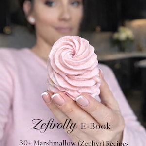 May include: A light pink, swirled marshmallow dessert is held in front of a person. The image includes text that reads "Zefirrolly E-Book" and "30+ Marshmallow (Zephyr) Recipes Classic & Author's Collection."