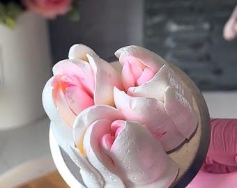 Può includere: Tre rose di crema al burro rosa e bianca su un piatto girevole argentato per decorare torte. Le rose sono disposte a grappolo e hanno un aspetto delicato e arricciato.