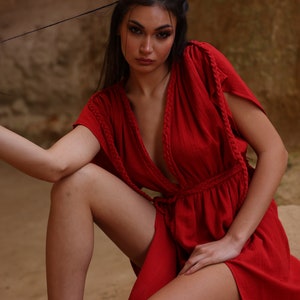 Puede incluir: Una mujer con un vestido rojo de manga larga, cuello en V profundo y detalle de cuerda trenzada. El vestido tiene un lazo en la cintura y una abertura en el lateral.
