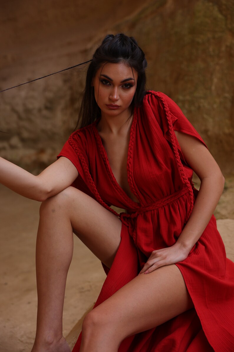 Puede incluir: Una mujer con un vestido rojo de manga larga, cuello en V profundo y detalle de cuerda trenzada. El vestido tiene un lazo en la cintura y una abertura en el lateral.
