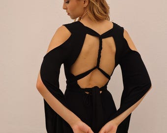 May include: A black dress featuring long, split sleeves that expose the shoulders. The back of the garment is open, showcasing a braided strap detail that connects the shoulder sections, with a tie closure at the waist and a flowing skirt.