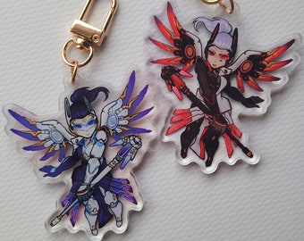 Puede incluir: Dos llaveros de personajes de Overwatch, uno con un diseño azul y morado y el otro con un diseño rojo y negro. Ambos llaveros representan a un personaje femenino con alas y un arma.