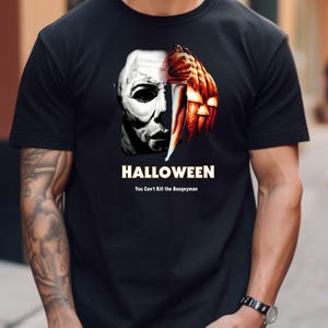 Könnte beinhalten: Schwarzes T-Shirt mit einem Halloween-Motiv. Die Grafik kombiniert eine Maske und einen geschnitzten Kürbis mit einem Messer. Das Wort "HALLOWEEN" steht über dem Text "You Can't Kill the Boogeyman".