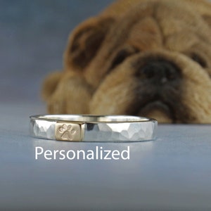 May include: A silver hammered band ring with a gold paw print inlay. The ring is personalized.