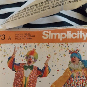K&ouml;nnte beinhalten: Eine Simplicity Schnittmusterh&uuml;lle 8773 mit zwei Clowns in bunten Kost&uuml;men und Konfetti-Grafiken. Die orangefarbene Kopfzeile zeigt den Markennamen und den Gr&ouml;&szlig;enbereich von XS bis XL. Das Design umfasst eine Weste, eine Fliege und einen R&uuml;schenkragen.
