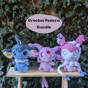 May include: Crochet pattern bundle featuring three amigurumi plushies: a blue Eevee, a purple Espeon, and a pink Umbreon. The plushies are sitting on a wooden shelf against a backdrop of green ivy.