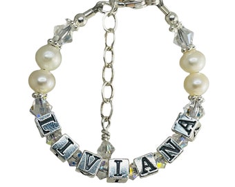 May include: A silver bracelet with a name spelled out in silver beads. The bracelet is made with clear crystals and white pearls.