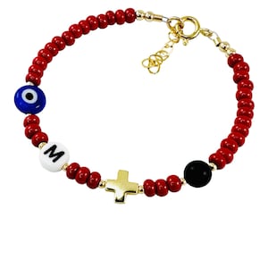 May include: Red beaded bracelet with a gold charm, a blue evil eye bead, a white bead with the letter "M", a gold cross charm, and a black bead.