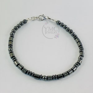 May include: A silver and black beaded bracelet with a silver clasp. The bracelet is made of small, round beads and larger, cylindrical beads.