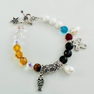 May include: A silver bracelet with a variety of charms, including a star, a cross, a fish, and a heart. The bracelet is made with white, black, and brown beads.