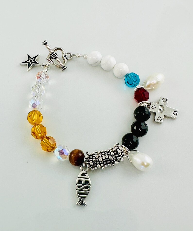 May include: A silver bracelet with a variety of charms, including a star, a cross, a fish, and a heart. The bracelet is made with white, black, and brown beads.