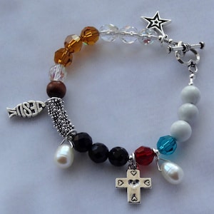 May include: A silver charm bracelet with a variety of beads, including clear, brown, black, white, red, and blue. The charms include a fish with the word "JESUS" on it, a cross with hearts, and a star.