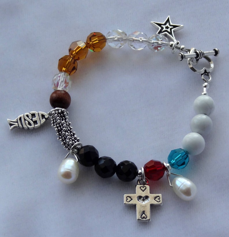 May include: A silver charm bracelet with a variety of beads, including clear, brown, black, white, red, and blue. The charms include a fish with the word "JESUS" on it, a cross with hearts, and a star.
