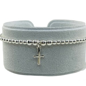 May include: A silver beaded bracelet with a small silver cross charm.