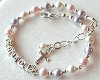 May include: A silver charm bracelet with a cross charm and a name spelled out in silver beads. The bracelet is made with white, pink, and gray pearls.