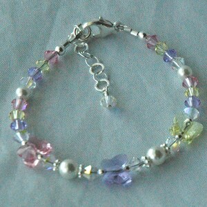 May include: A delicate bracelet with a silver chain and colorful crystal beads. The beads are arranged in a rainbow pattern, with shades of pink, purple, yellow, and green.