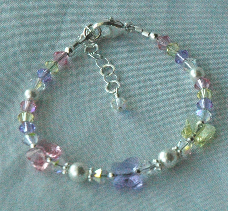 May include: A delicate bracelet with a silver chain and colorful crystal beads. The beads are arranged in a rainbow pattern, with shades of pink, purple, yellow, and green.