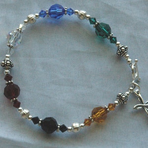 May include: A silver bracelet with a cross charm features a variety of colored glass beads, including clear, blue, green, brown, red, and black.